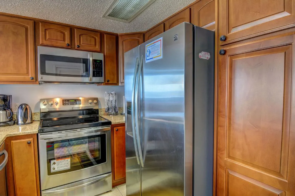 This photo offers a clear view of the stainless steel refrigerator, modern oven, granite countertop, and abundant wooden cabinetry. The kitchen is thoughtfully arranged for both practicality and comfort, making it ideal for anything from quick snacks to elaborate meals.