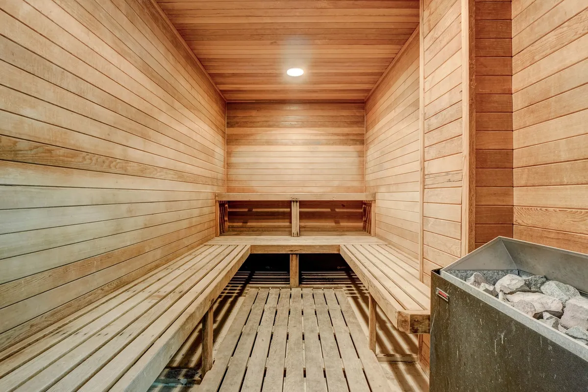 A serene interior sauna with wooden benches, wood-paneled walls, and a sauna heater. The calming ambiance suggests a space for relaxation and post-workout recovery.