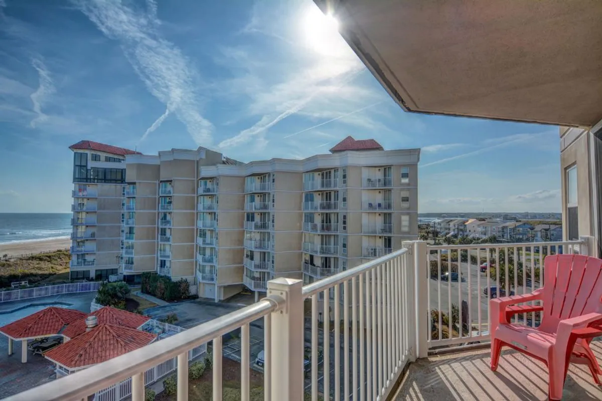 A private balcony scene featuring a red chair overlooking the vast ocean, with nearby buildings framing the view. The tranquil setting invites relaxation and enjoyment of the ocean vistas, whether for morning coffee or evening wine as described in the section.
