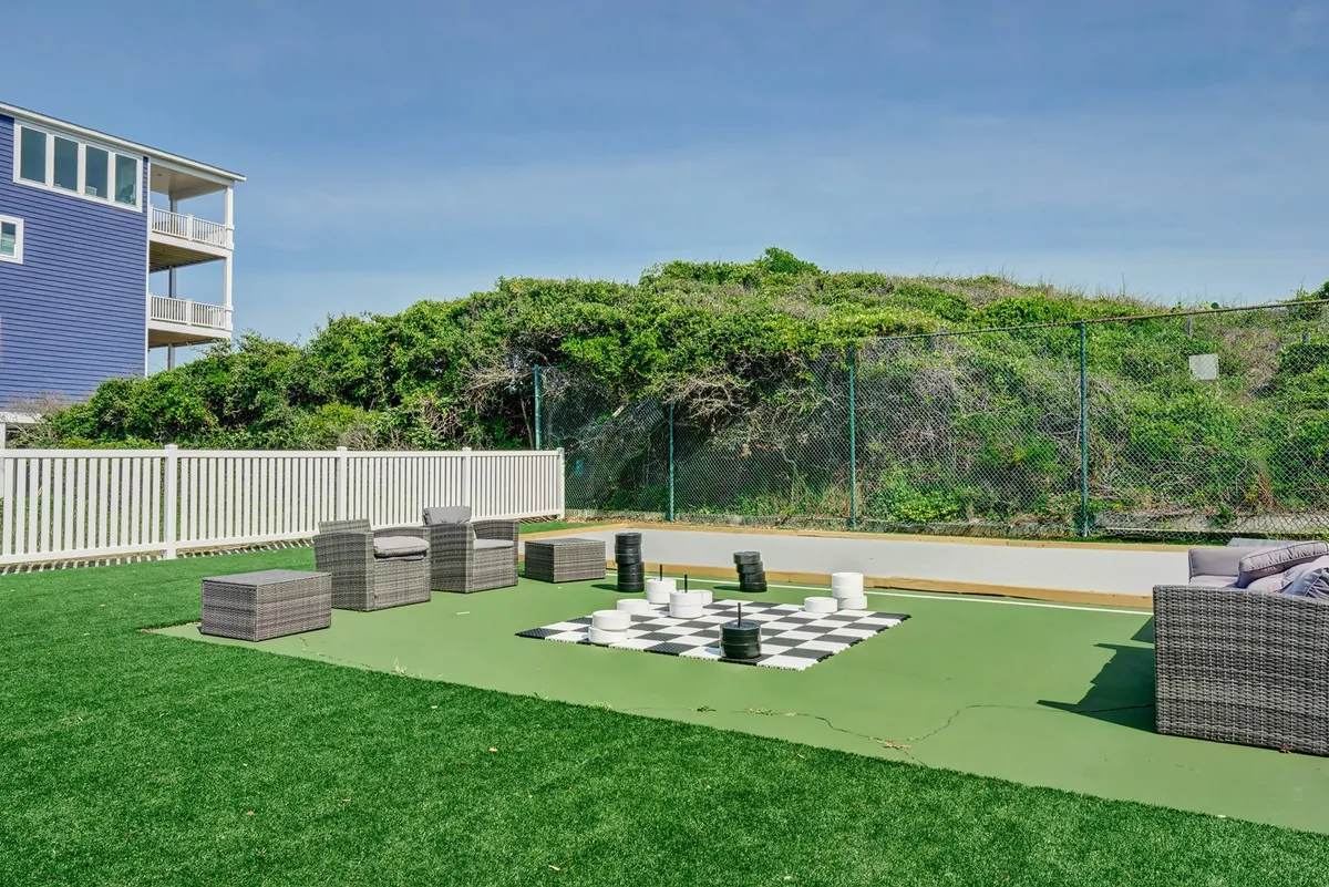 A vibrant outdoor setting featuring a large chessboard on a green lawn, surrounded by comfortable seating areas perfect for gatherings. The playful atmosphere is ideal for socializing and friendly competition, with lush grass and open space inviting groups to enjoy time together.